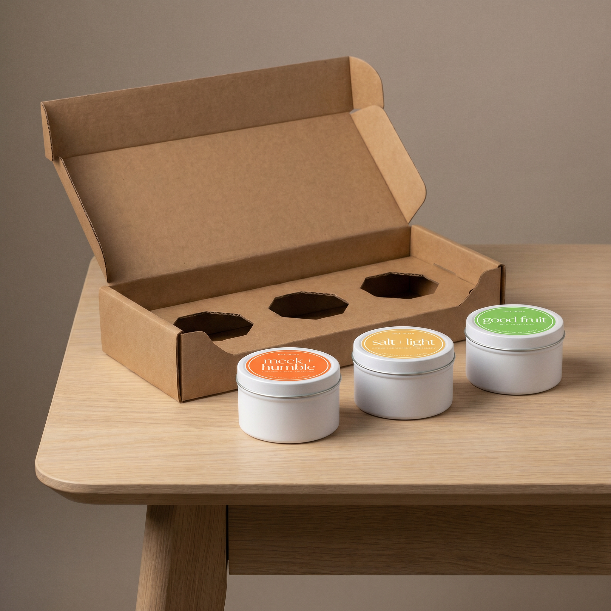 Three small metal containers with colorful labels on a wooden table next to an open cardboard box.