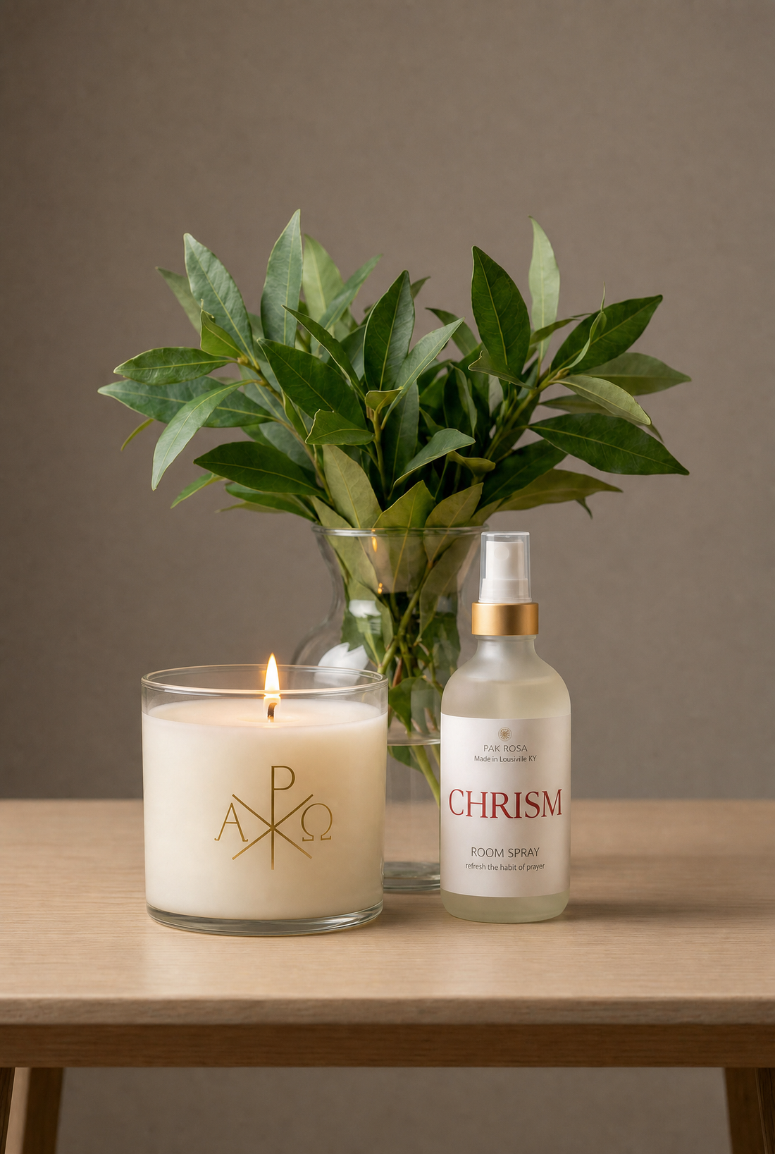 Candle, bottle of perfume, and vase with green leaves on a wooden table against a brown background