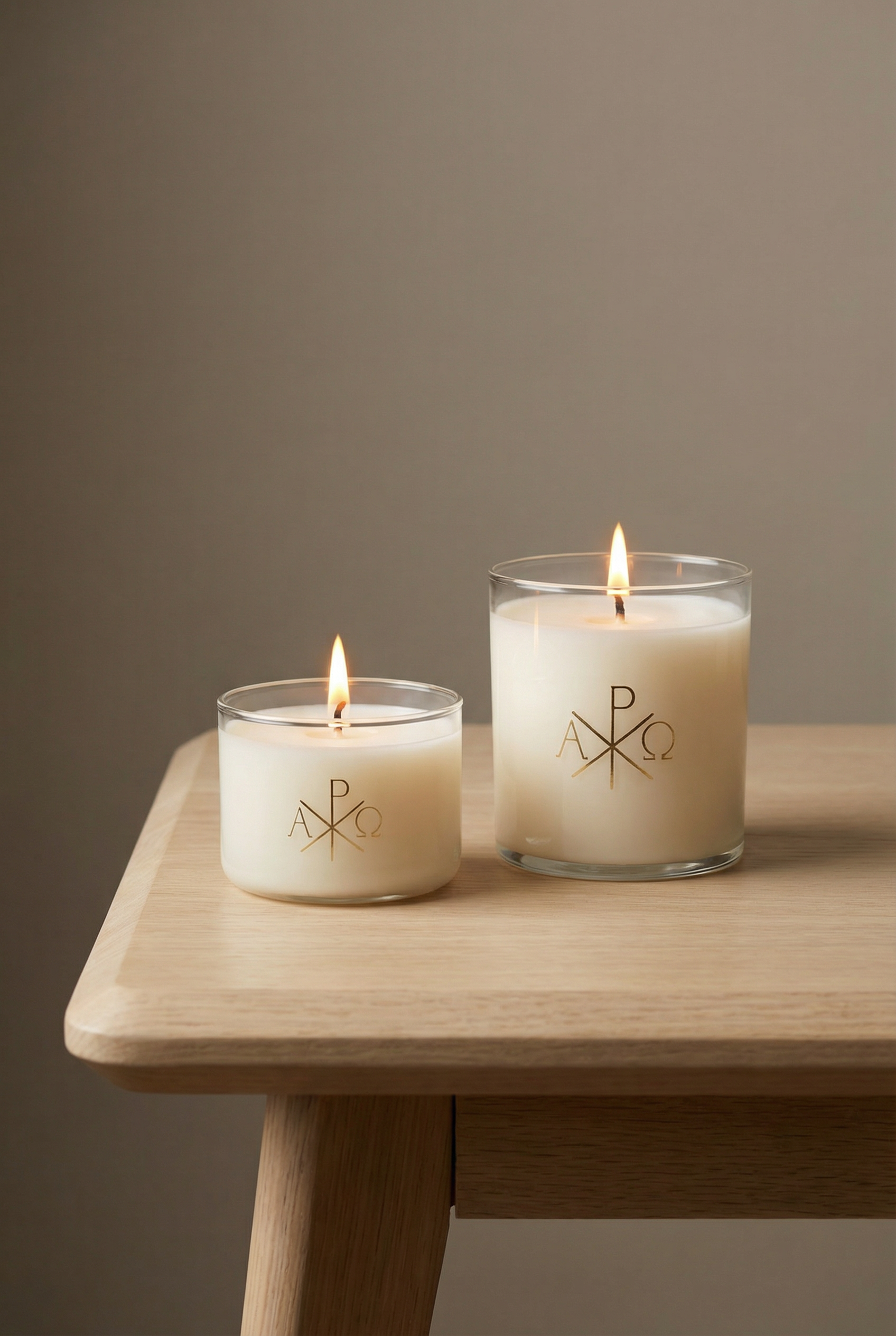 Two lit candles with a logo on a wooden table against a plain background