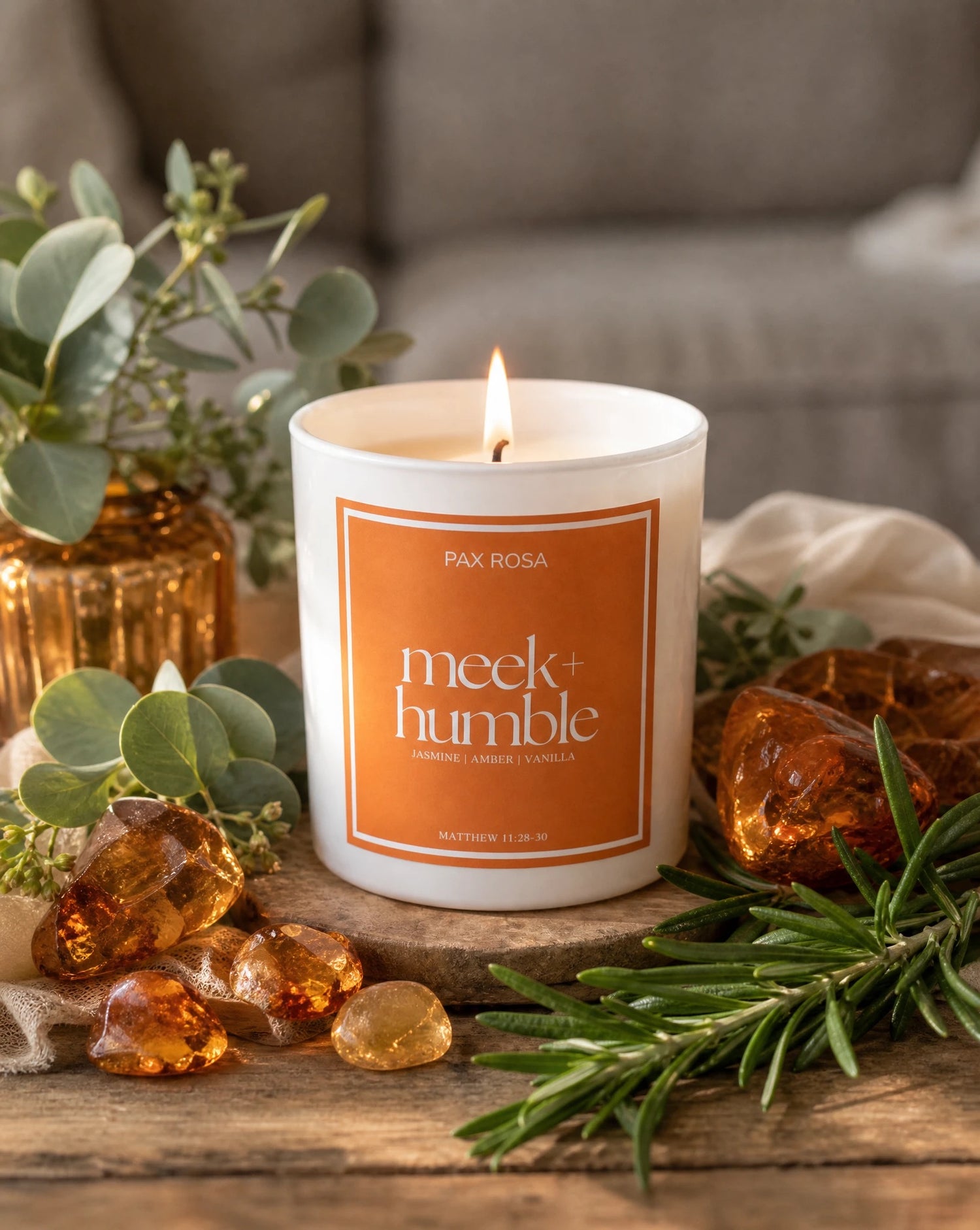 candle reading "Meek and Humble" sitting on a table with pieces of amber and greenery