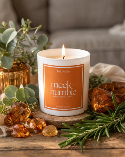candle reading "Meek and Humble" sitting on a table with pieces of amber and greenery