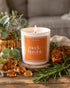 candle reading "Meek and Humble" sitting on a table with pieces of amber and greenery
