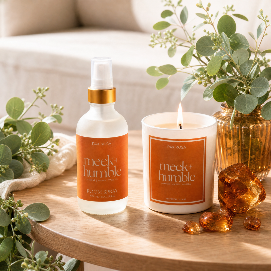 Meek Humble products including a bottle and candle on a wooden table with plants.