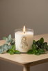 Candle with a figurine design on a wooden surface with green leaves